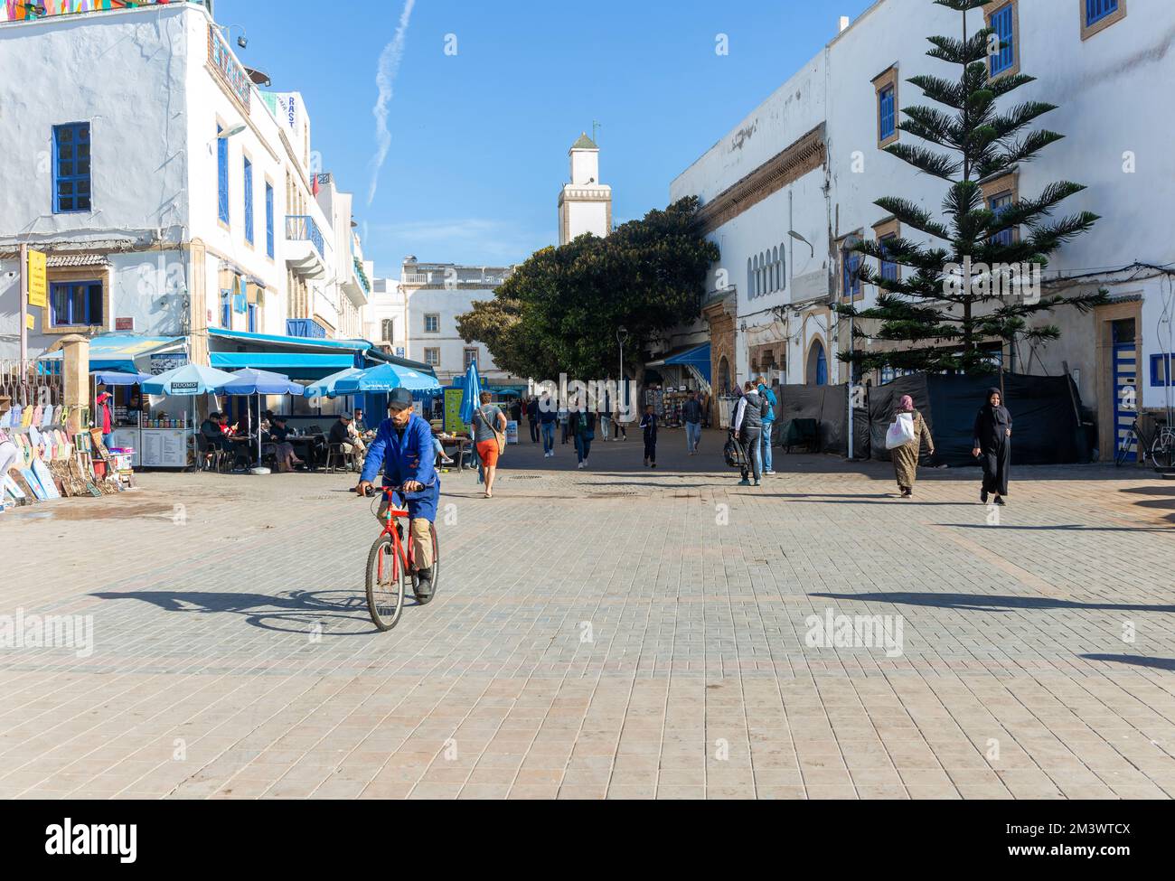 People walking man cycling, Place Moulay Hassan, Essaouira, Morocco, north Africa Stock Photo