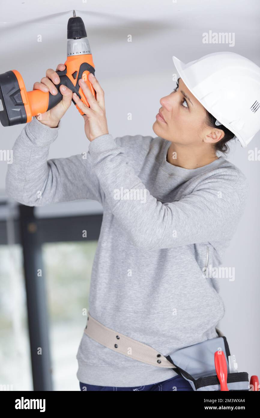 happy female worker drilling ceiling Stock Photo