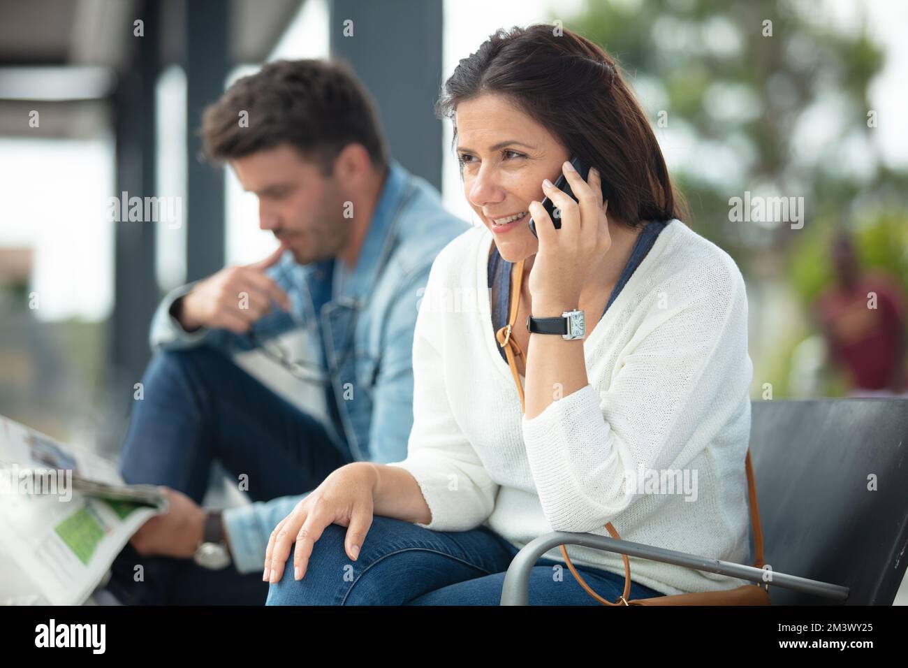 couple waiting at bus-stop reading and using smartphone Stock Photo