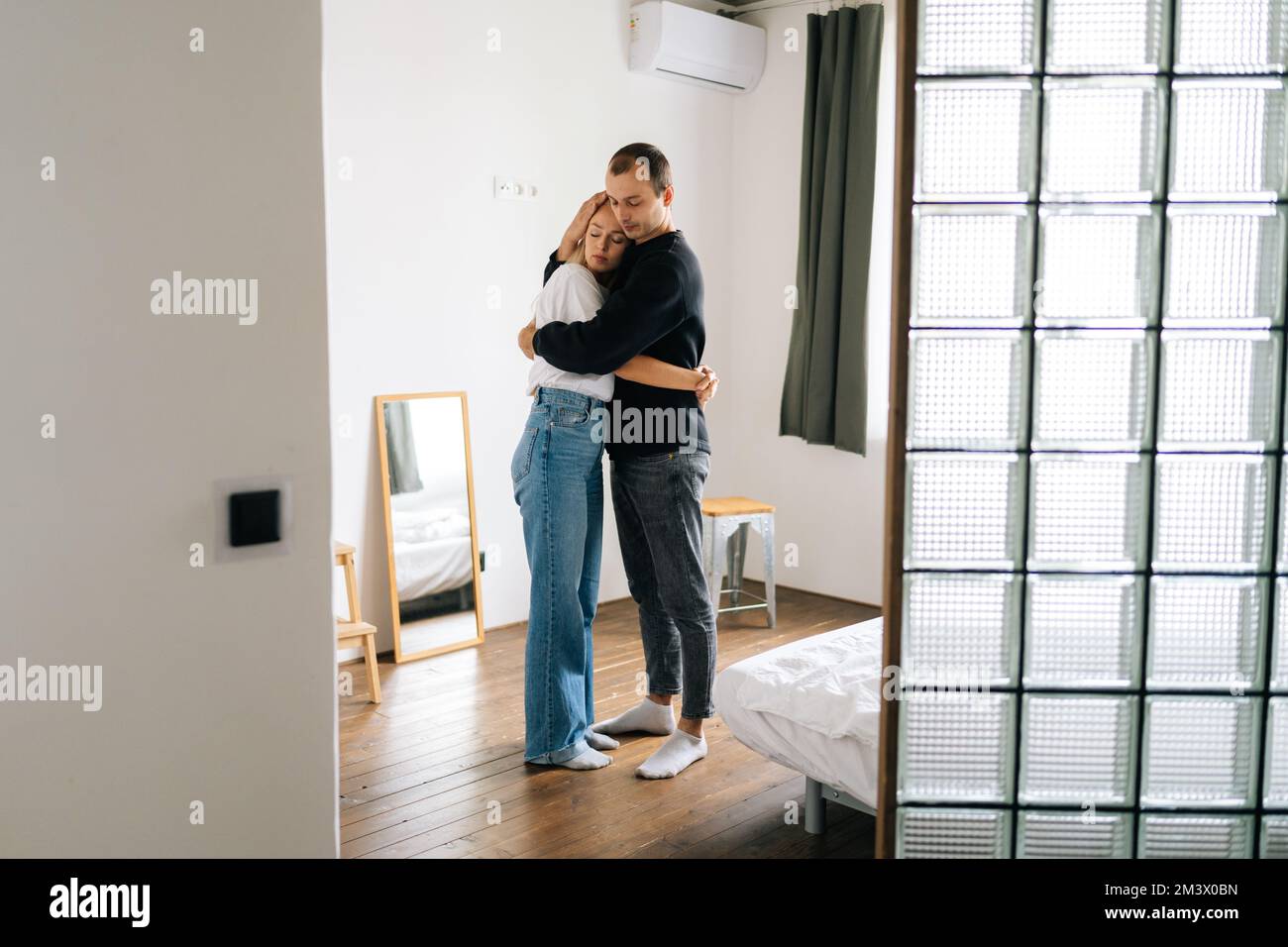 Portrait of sad young couple having relationship trouble, embracing emotional issues, sharing bad news at home. Loving man and woman consoling each Stock Photo