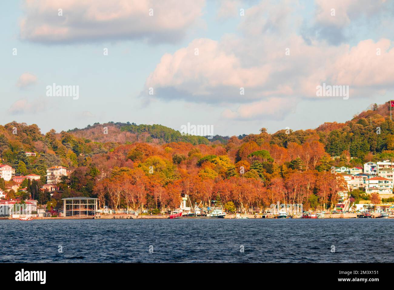 View of Beykoz beach from the sea. Trees clad in autumn colors in Beykoz. Cloudy blue sky. Landscape. No people, nobody. Horizontal photo. Stock Photo
