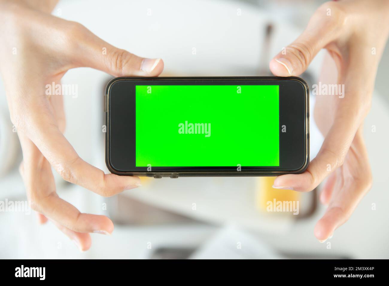closeup hand holding smartphone top view in restaurant with blank space green screen colored Stock Photo