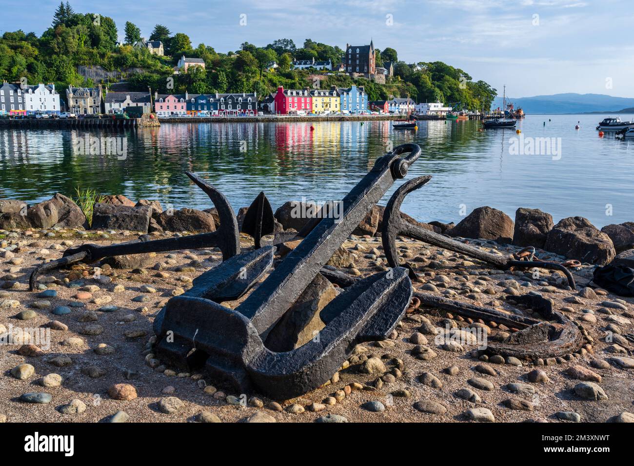 Anchors on the quayside with distant view of colourful houses on the waterfront of Tobermory, Isle of Mull, Scotland, UK Stock Photo