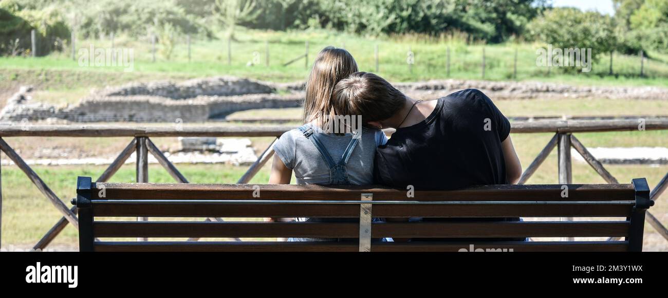 Horizontal banner or header with back view of a young gen z couple sitting on a bench at the campus park Stock Photo