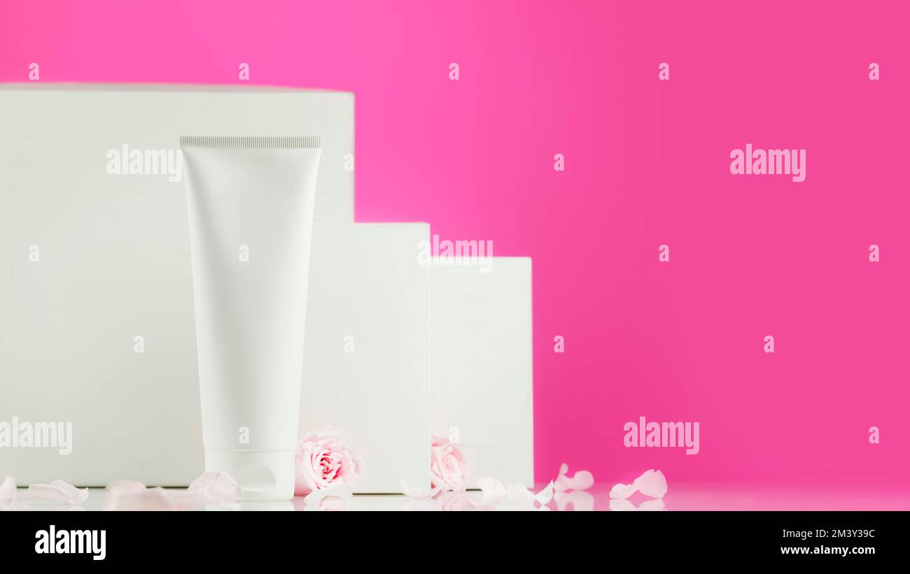 Mock up of natural beauty products based on rose flowers. White cosmetic tube with white boxes on pink background with tender pink roses, rose petals Stock Photo