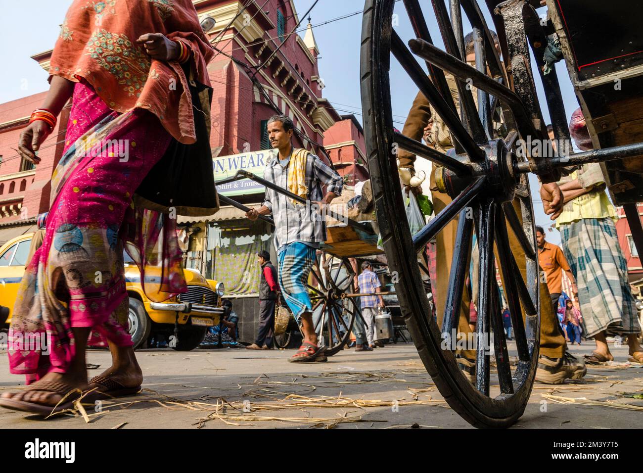 Wheel of a pull rikshaw, another rikshaw kuli and more people behind ...