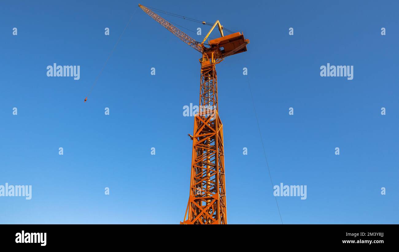 Tall high mechanical yellow mobile crane for construction engineering purposes into blue sky. Stock Photo