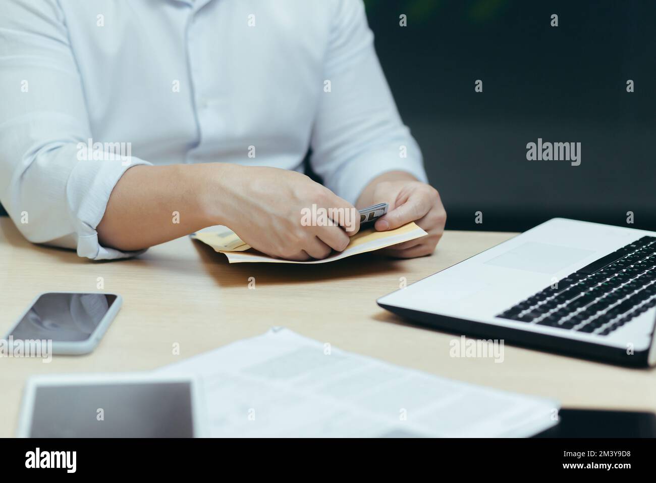 Close-up photo. A man's hands at a table with a laptop and documents take out cash from an envelope, count money. Stock Photo