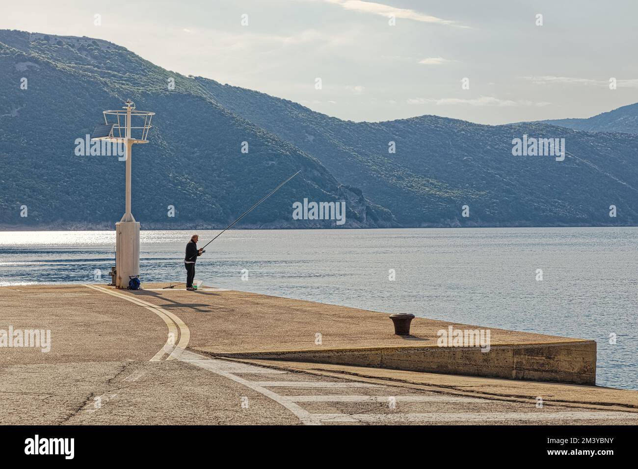 Fisherman catches fish with a fishing rod in Porozina port Stock Photo ...