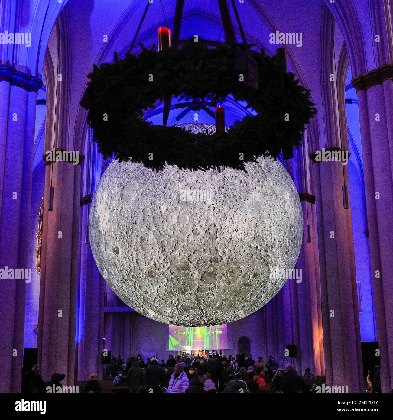 Münster, Germany. 17th Dec, 2022. A Christmas wreath hangs parallel to the installation, making it look like a halo from some angles. People visit the 7-metre diameter illuminated 'Museum of the Moon' installation by British artist Luke Jerram at Überwasserkirche, a gothic church in the centre of Münster's old town. Queues have formed outside the church and the installation clearly proves popular with the many visitors to the historic town. Credit: Imageplotter/Alamy Live News Stock Photo