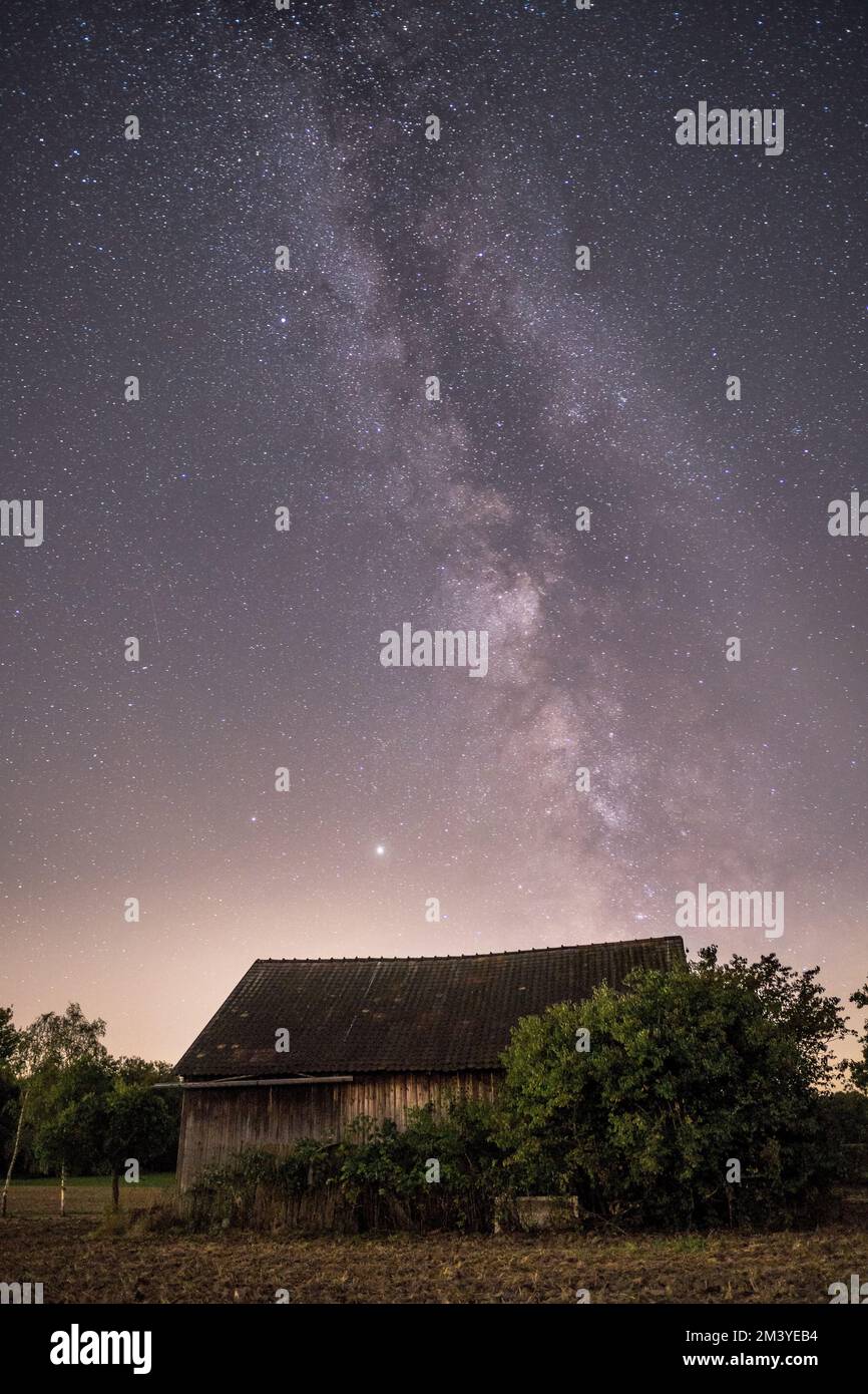 A vertical shot of the Milky Way and the starry sky over a small rural ...