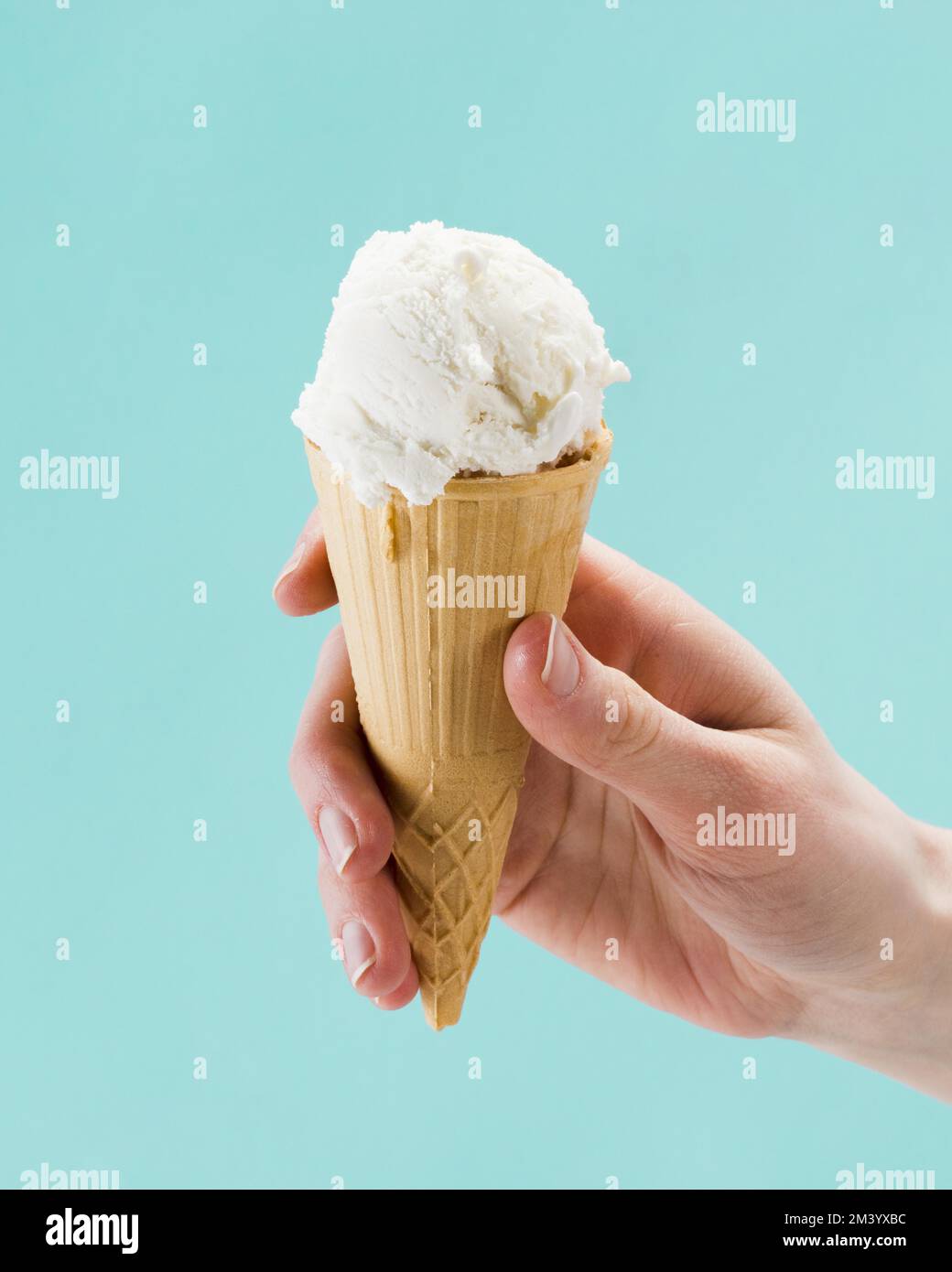 Hand holding vanilla ice cream cone blue background Stock Photo - Alamy