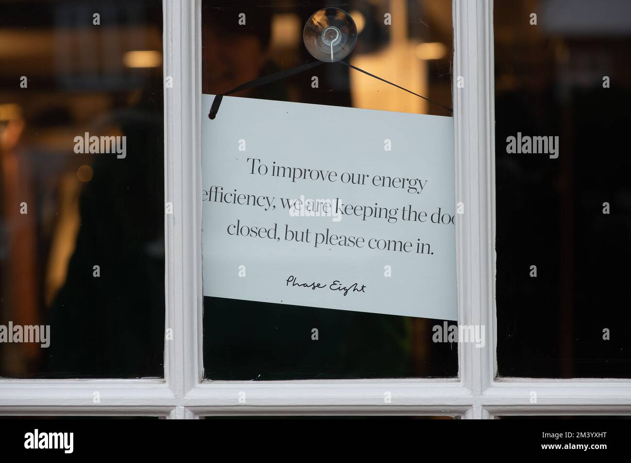 Old Amersham, Buckinghamshire, UK. 17th December, 2022. A notice on the door of Phase Eight tells customers to improve the energy efficiency that they are keeping the door closed. Credit: Maureen McLean/Alamy Live News Stock Photo