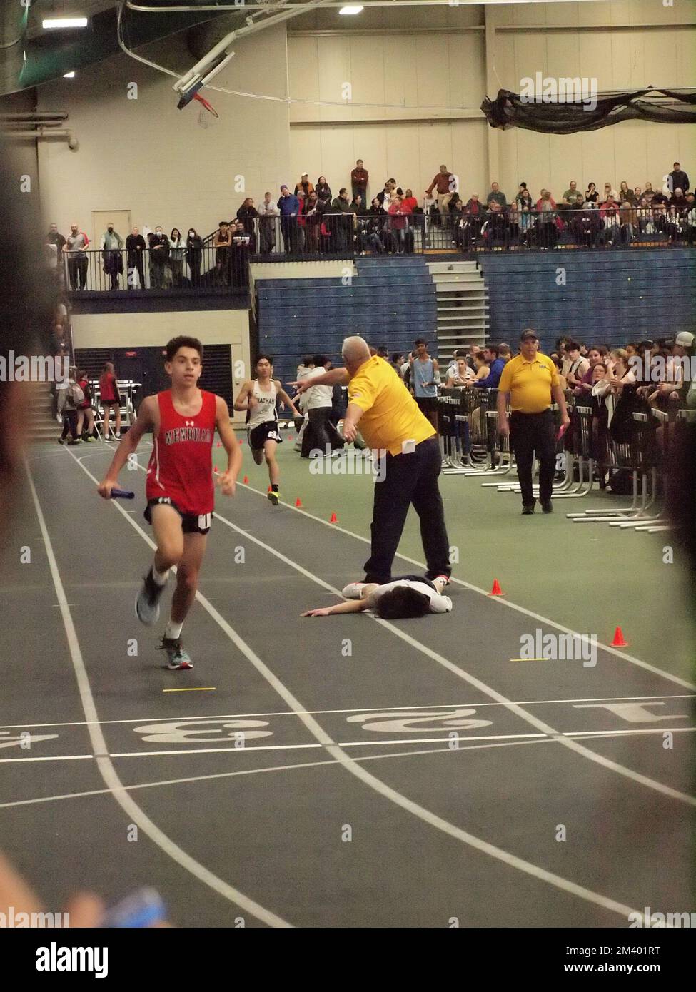 Runner at a New Jersey indoor track and field competition, collapses near finish line. First responders rendering aid to the teen male. Stock Photo