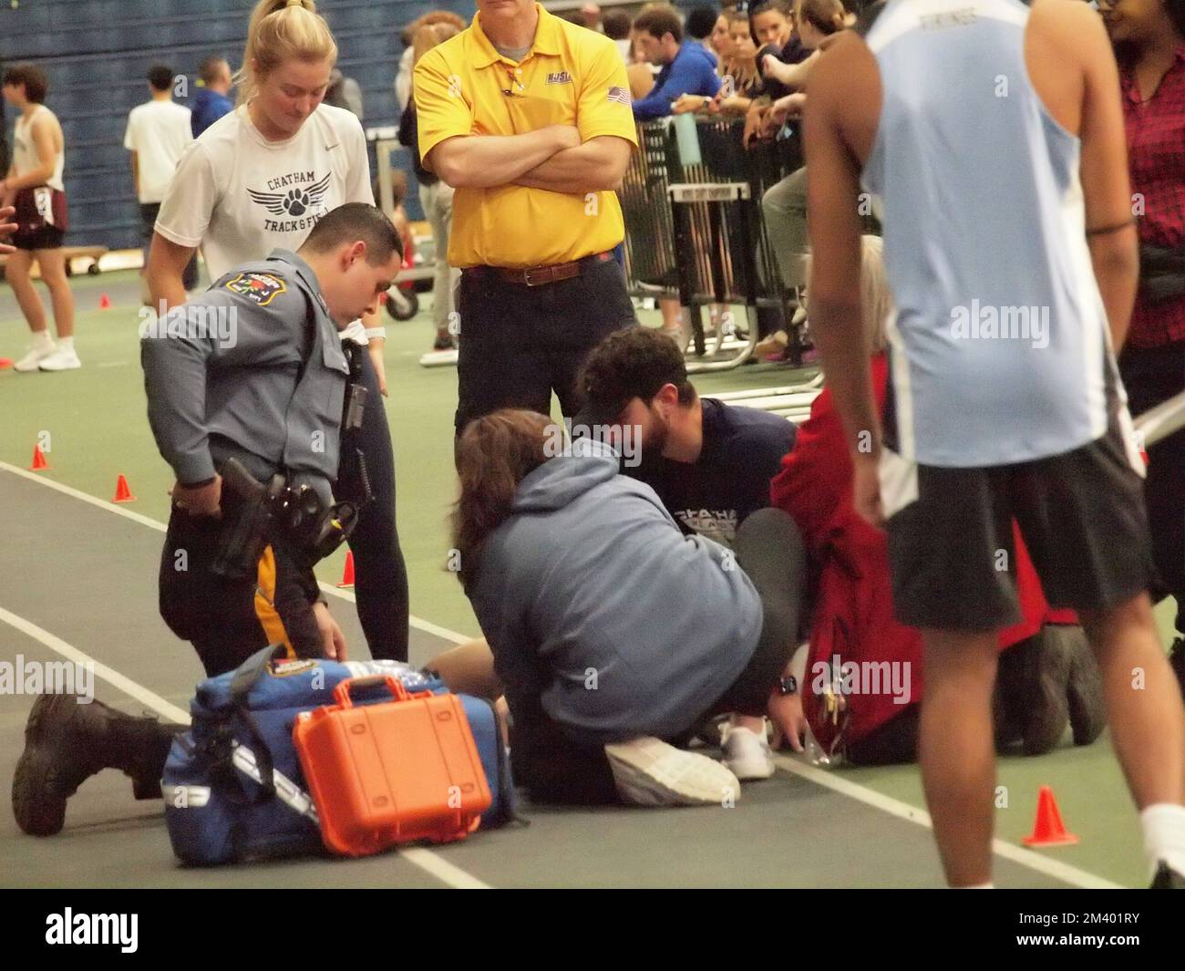 Runner at a New Jersey indoor track and field competition, collapses near finish line. First responders rendering aid to the teen male. Stock Photo