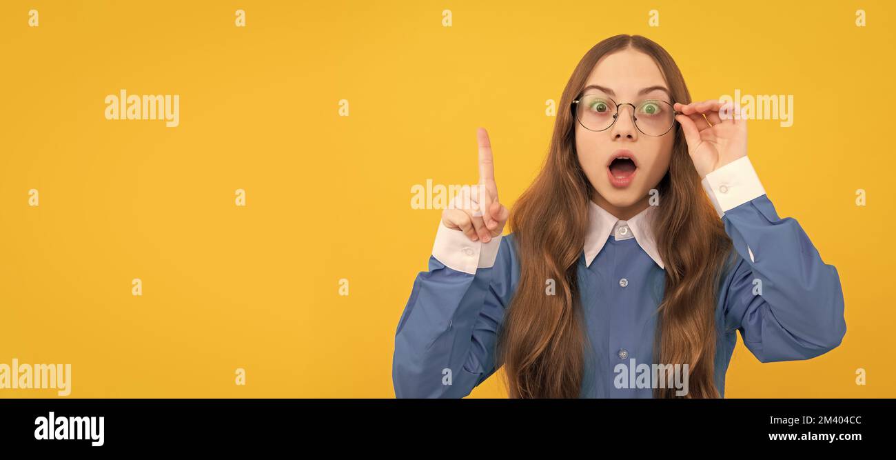 Shocked teenage girl in eyeglasses got genius idea keeping raised finger yellow background, clever. Child face, horizontal poster, teenager girl Stock Photo