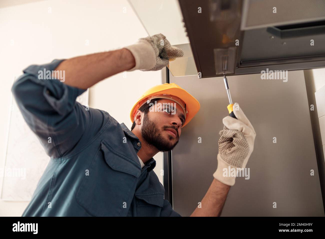 Handyman in uniform repairing kitchen extractor, replacing filter in