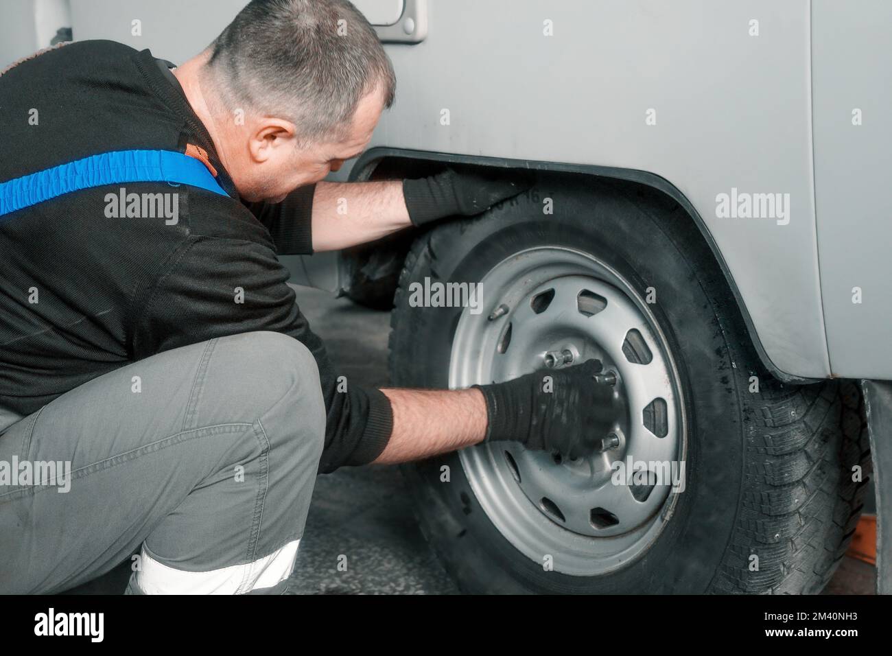 Man changes wheel of car in car service. Professional auto mechanic in overalls removes wheel from truck in garage. Authentic workflow.. Stock Photo