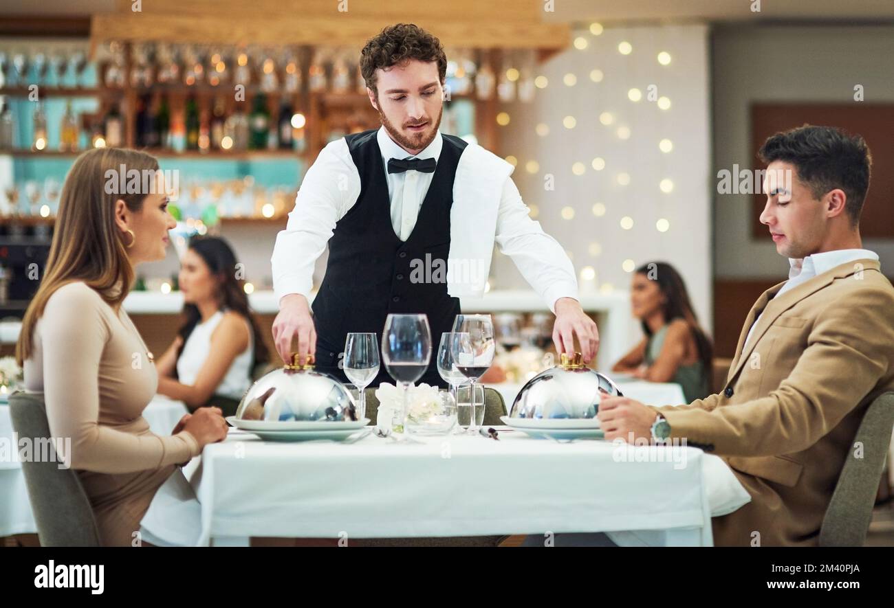 Allow me to serve you. a handsome young waiter serving a young couple