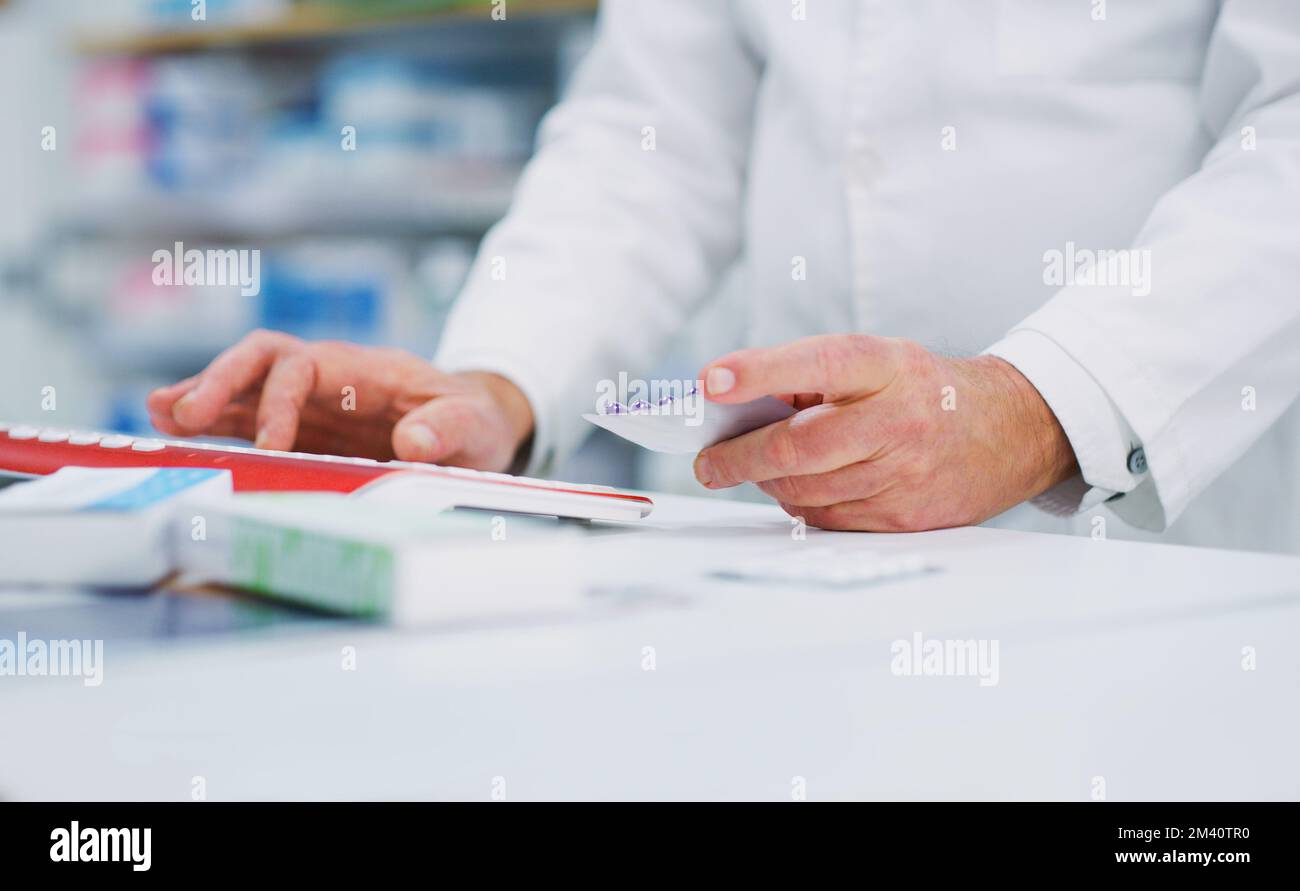 Im extra careful when distributing dosages. a pharmacist holding medication while typing on a computer. Stock Photo