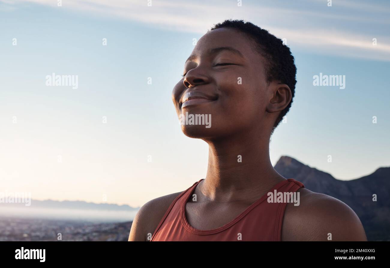 Fitness, calm and breathing of black woman outdoor in nature, mountains and blue sky background for yoga wellness, meditation and zen energy. Face of Stock Photo
