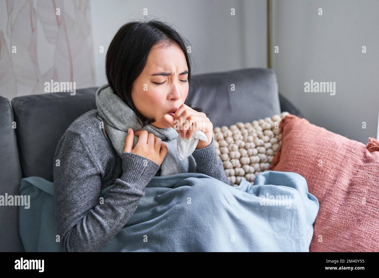 Asian woman coughing, feeling sick, sitting under blanket with scard in