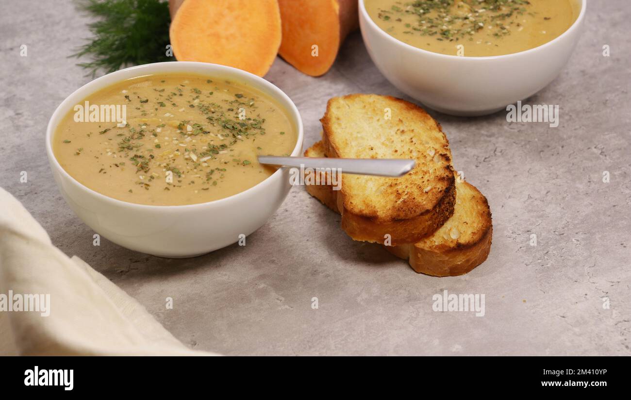 sweet potato puree soup in white bowl with garlic bread on grey marble