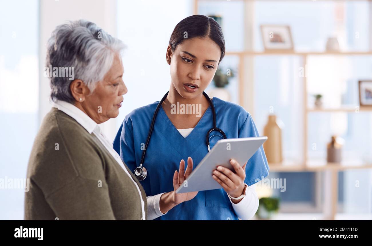 Taking her through her diagnosis. a young doctor using a digital tablet during a consultation with a senior woman. Stock Photo