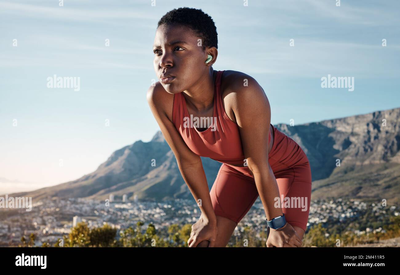 Tired, music and mountain with black woman running in nature for sport, endurance and breathing. Podcast, streaming and mobile radio with runner Stock Photo
