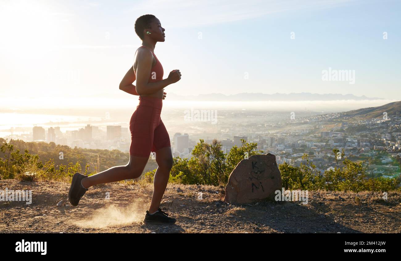 Woman, runner and fitness on mountain with music for wellness workout or cardio training with audio motivation. Black woman, athlete and listening or Stock Photo