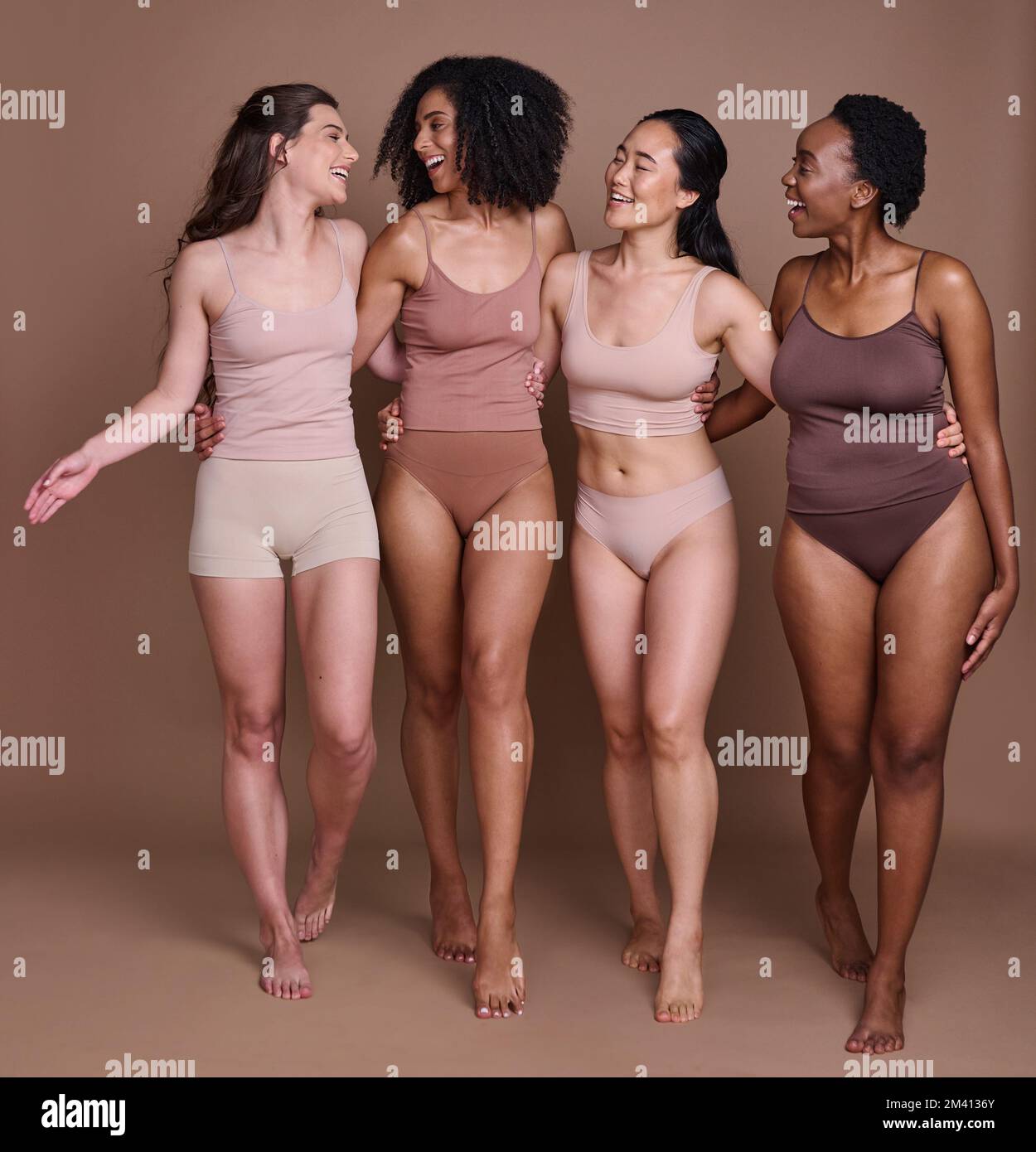 Four smiling women of different ages embracing their natural and aging  bodies. Four happy and body positive women embracing each other while  wearing red underwear against a studio background. stock photo