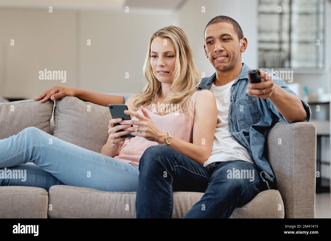 Curious, jealous and couple watching tv with a phone, social media and movie on living room sofa. Relax, jealousy and man reading communication on Stock Photo