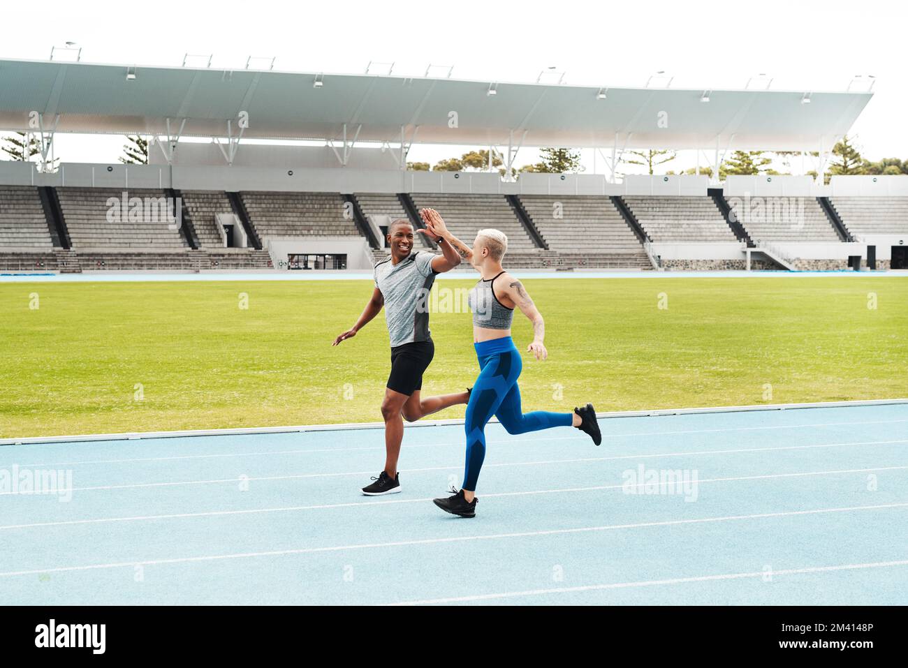 You did great. Full length shot of two young athletes giving each other a high five during a run on a track field. Stock Photo
