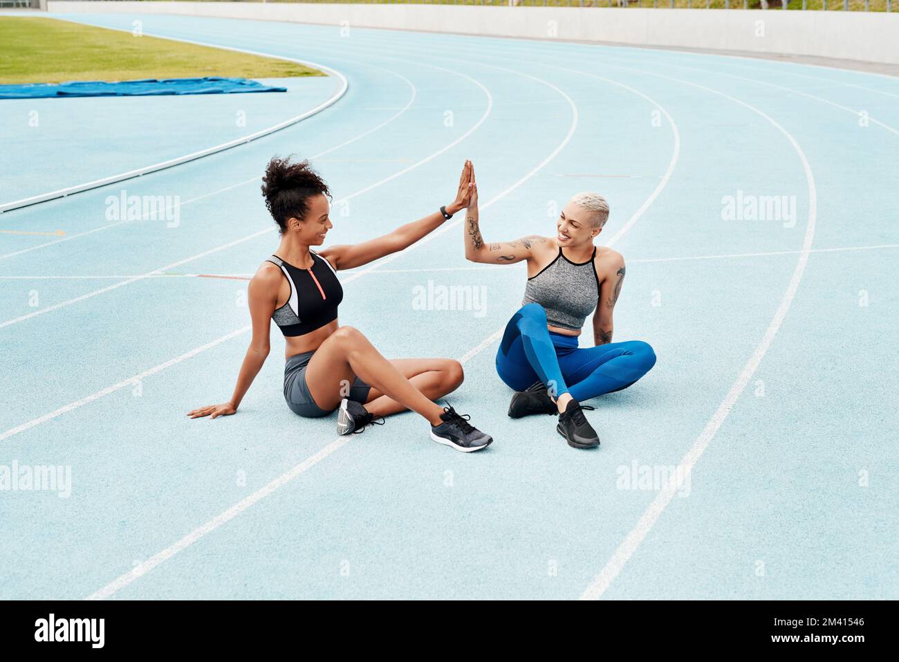 Lets do this. Full length shot of two attractive young athletes sitting together and giving each other a high five after running. Stock Photo