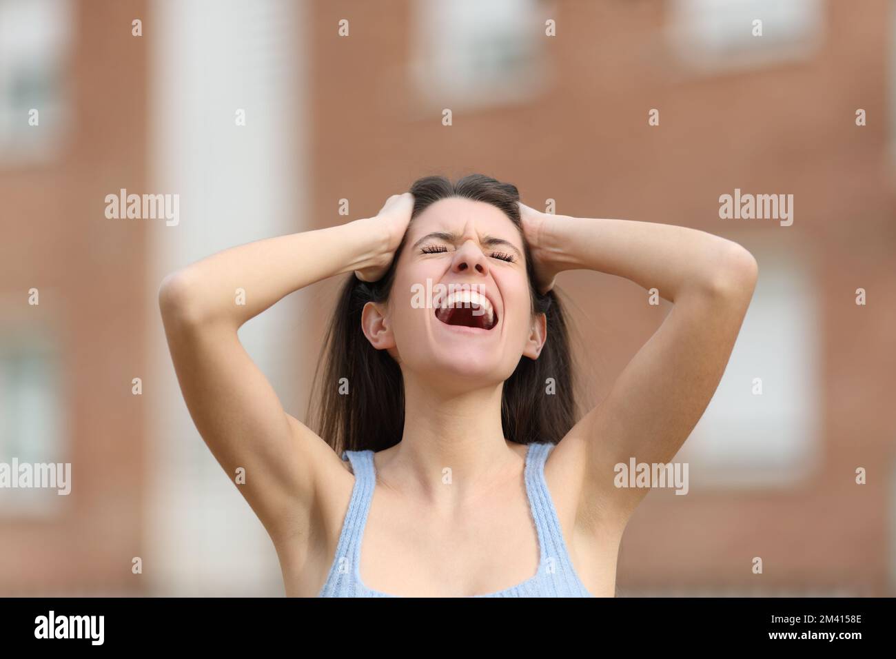 Desperate woman yelling with hands on head in the street Stock Photo