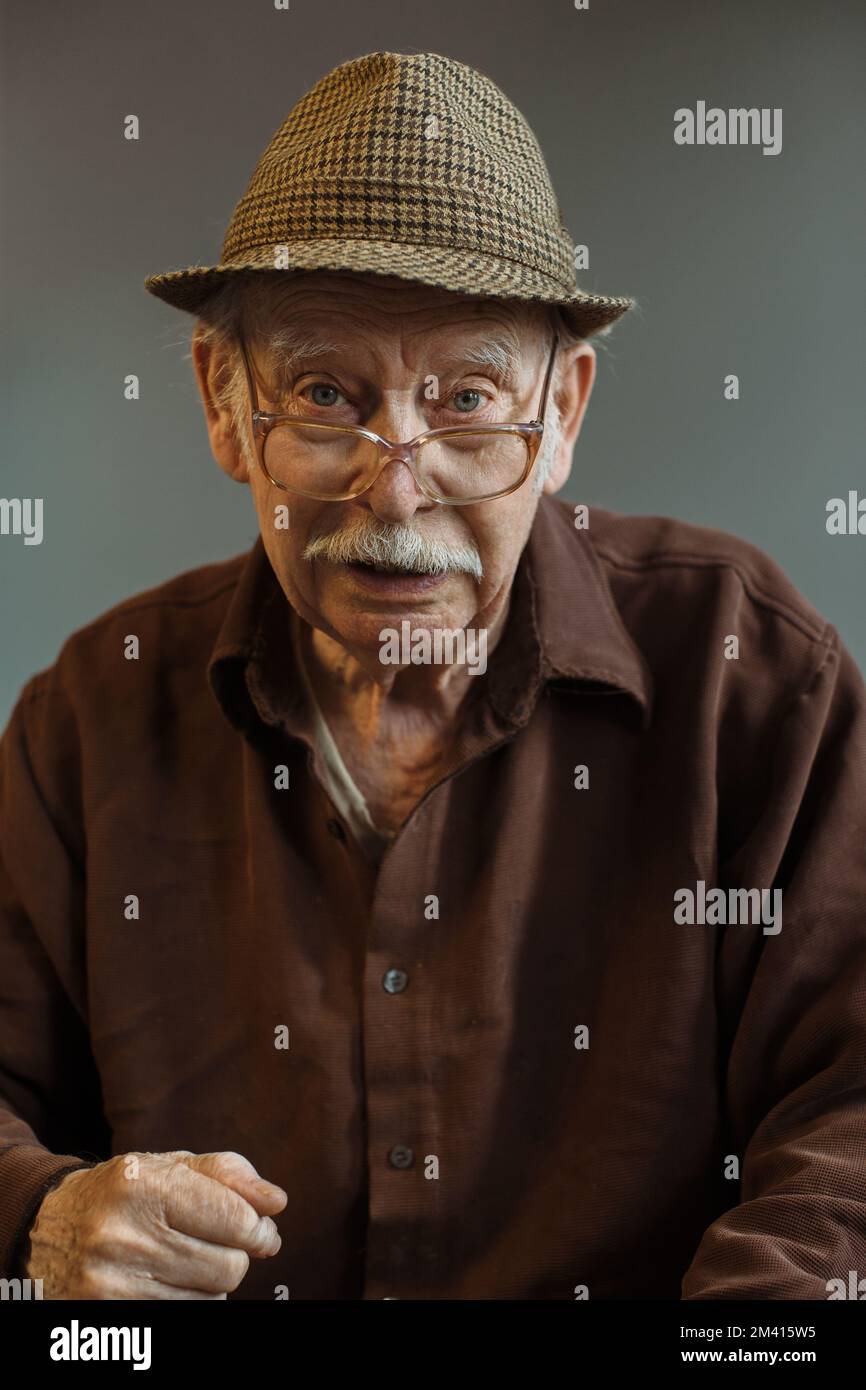 The old generation. Portrait of a senior man in glasses and a hat on a gray background. Stock Photo