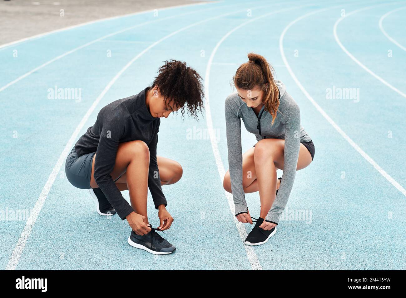 Laces tied, lets go. Full length shot of two attractive young athletes crouching together and tying their shoelaces before running on a track. Stock Photo