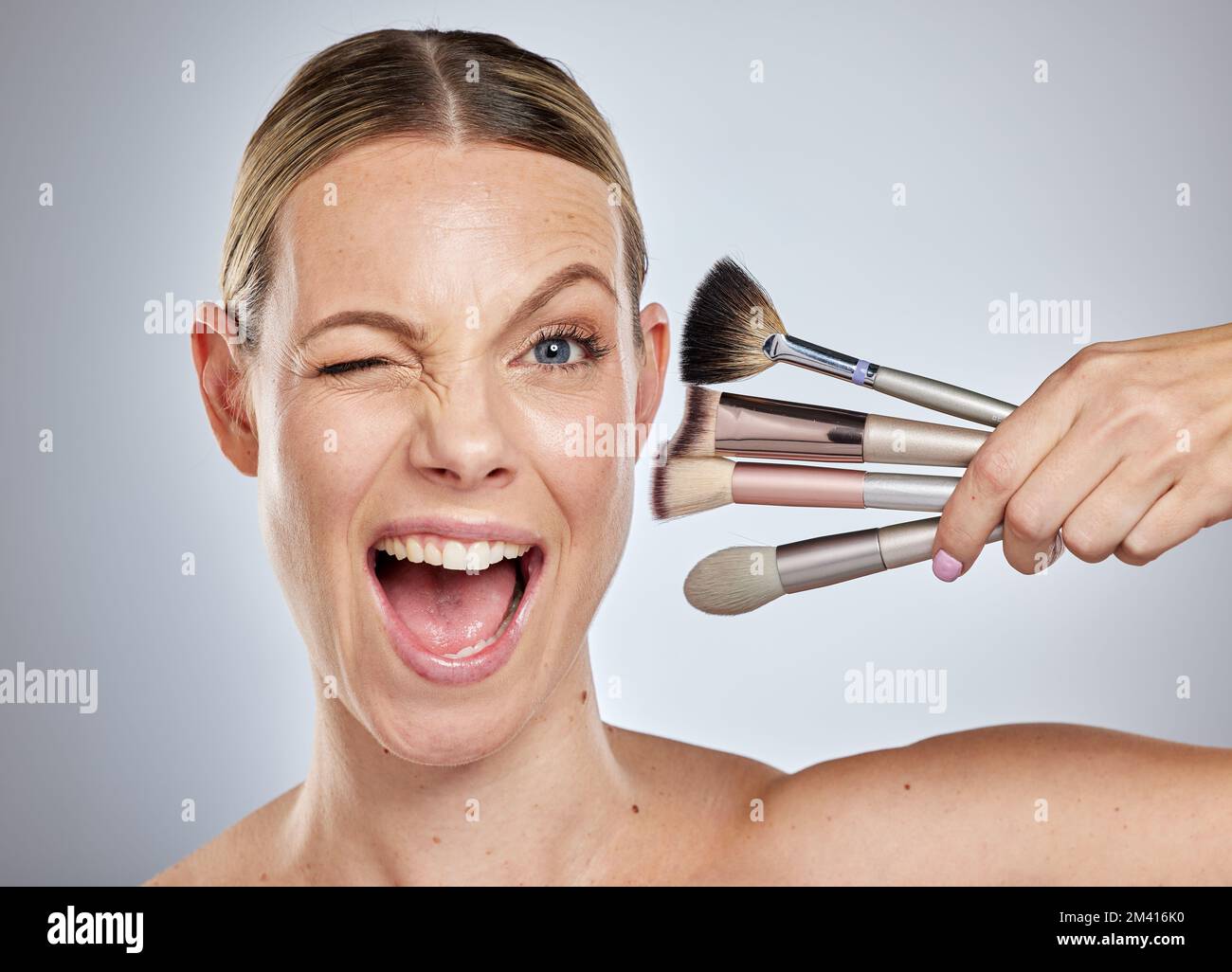 Woman, face and wink with makeup brushes for cosmetics or facial ...