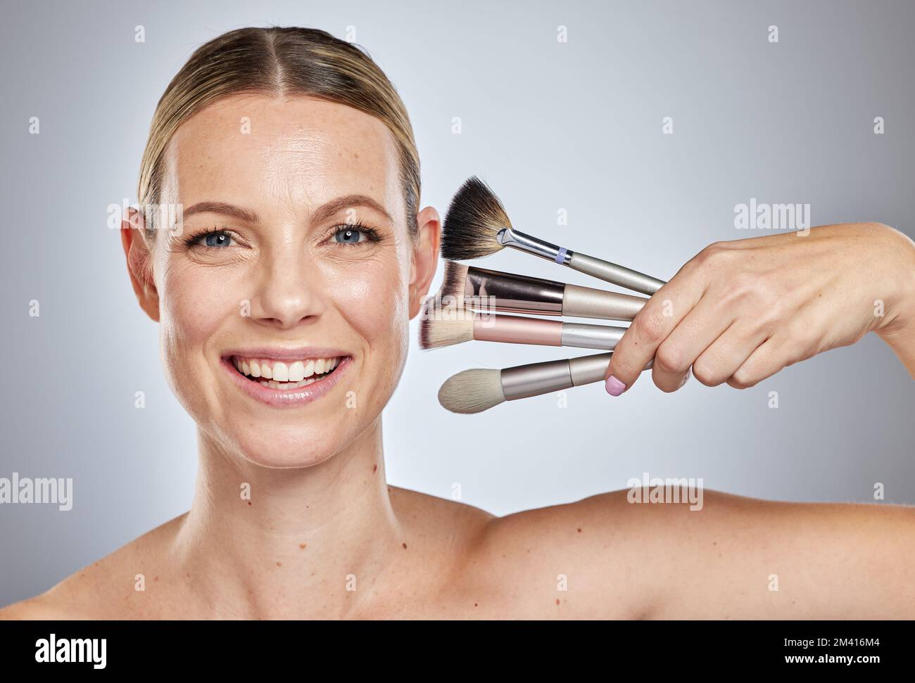 Woman, makeup brushes and portrait smile for cosmetics, beauty or facial treatment against a studio background. Happy face of female model smiling in Stock Photo