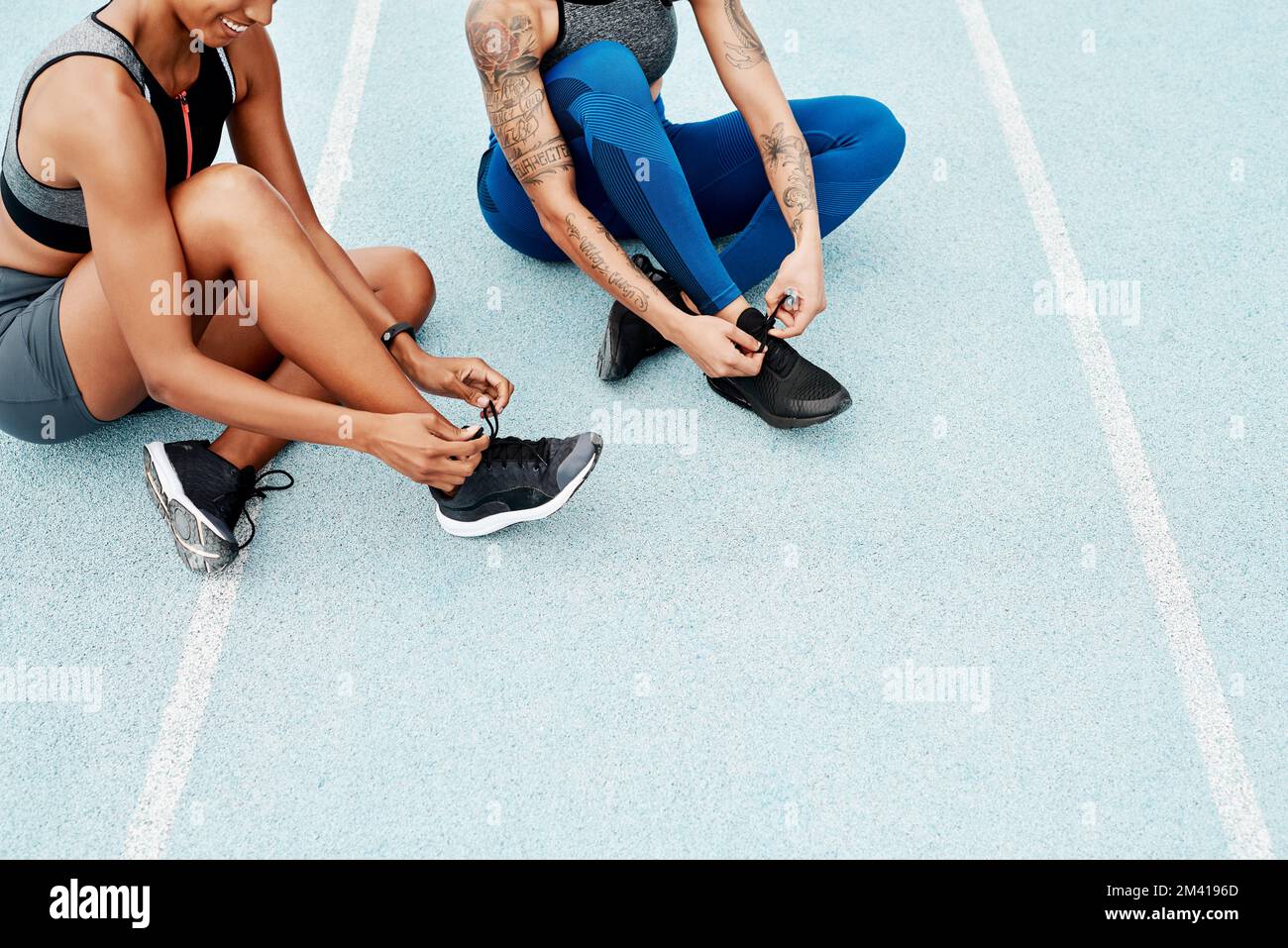 Have to make sure our laces are tied. two attractive young athletes sitting together and tying their shoelaces before running on a track. Stock Photo