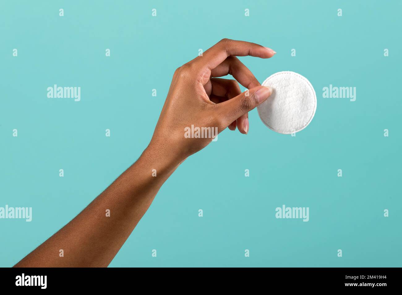 Crop black female demonstrating clean cotton pad for makeup removal against turquoise background Stock Photo