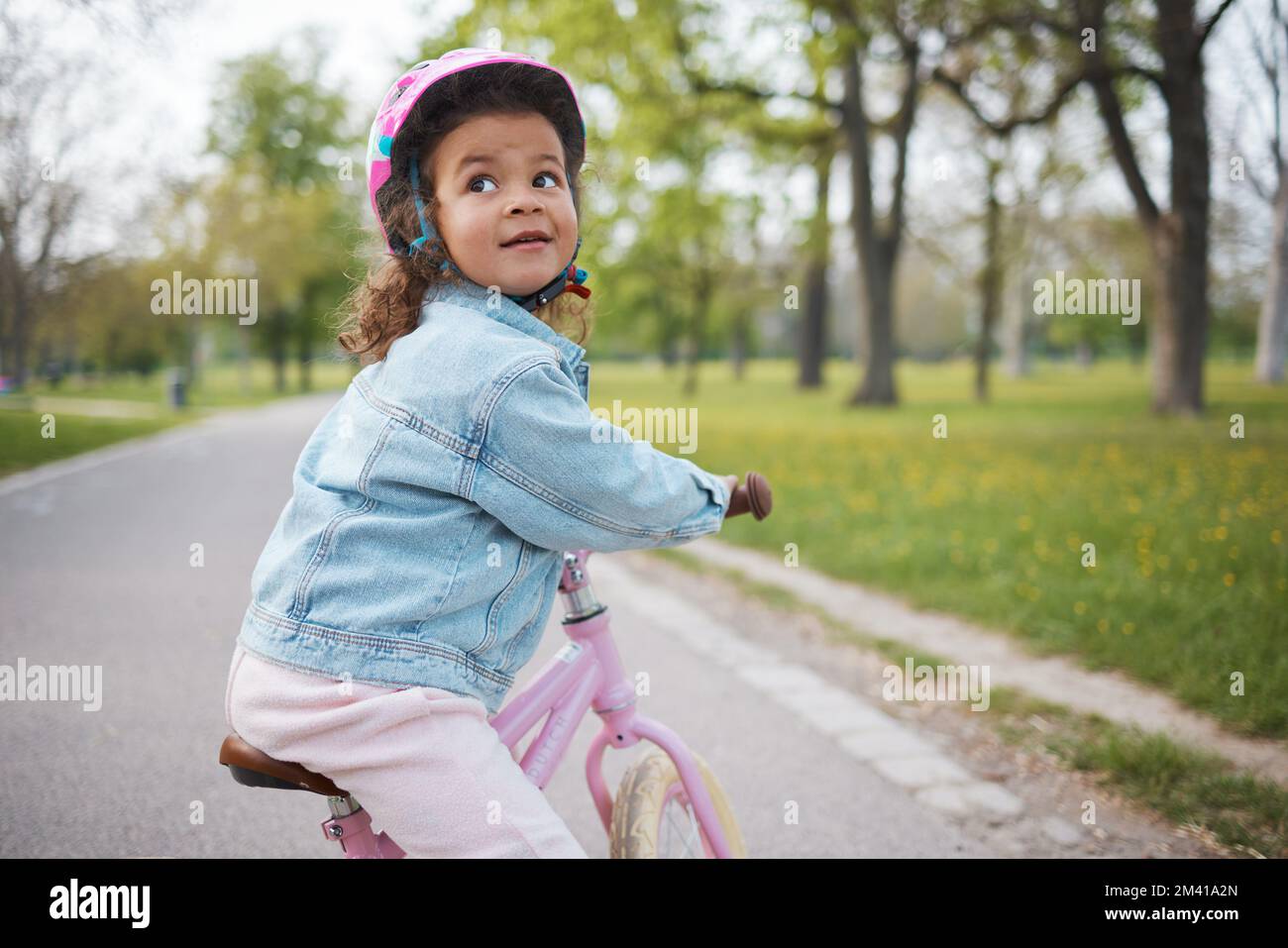 Kids, bike and learning to ride with a girl in the park on her bicycle while wearing a helmet for safety outdoor. Summer, cycling and children with a Stock Photo