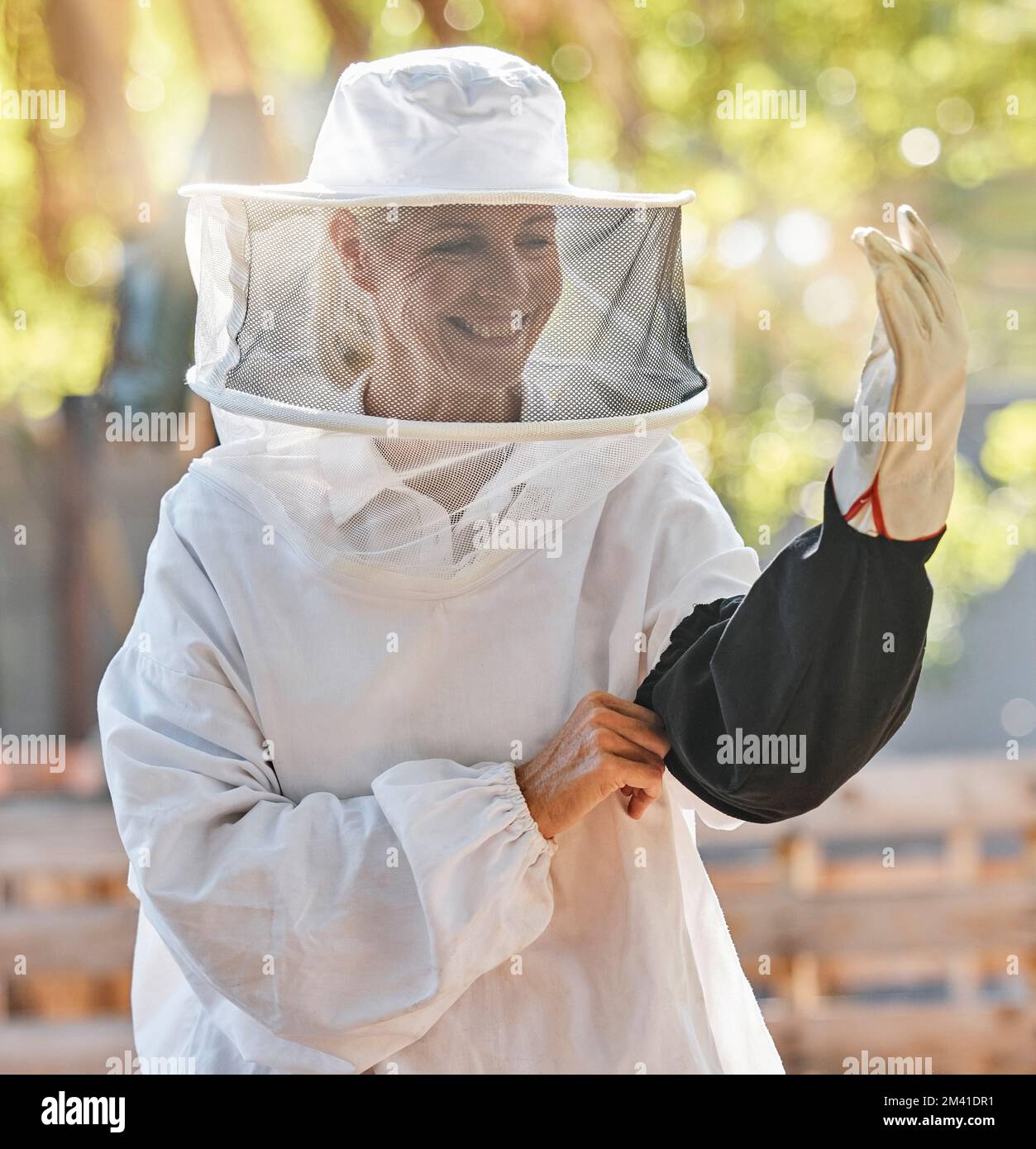 Beekeeper woman, smile and safety at farm with apiculture suit, vision or happy in summer harvesting time. Bee expert, ppe clothes or happiness in eco Stock Photo
