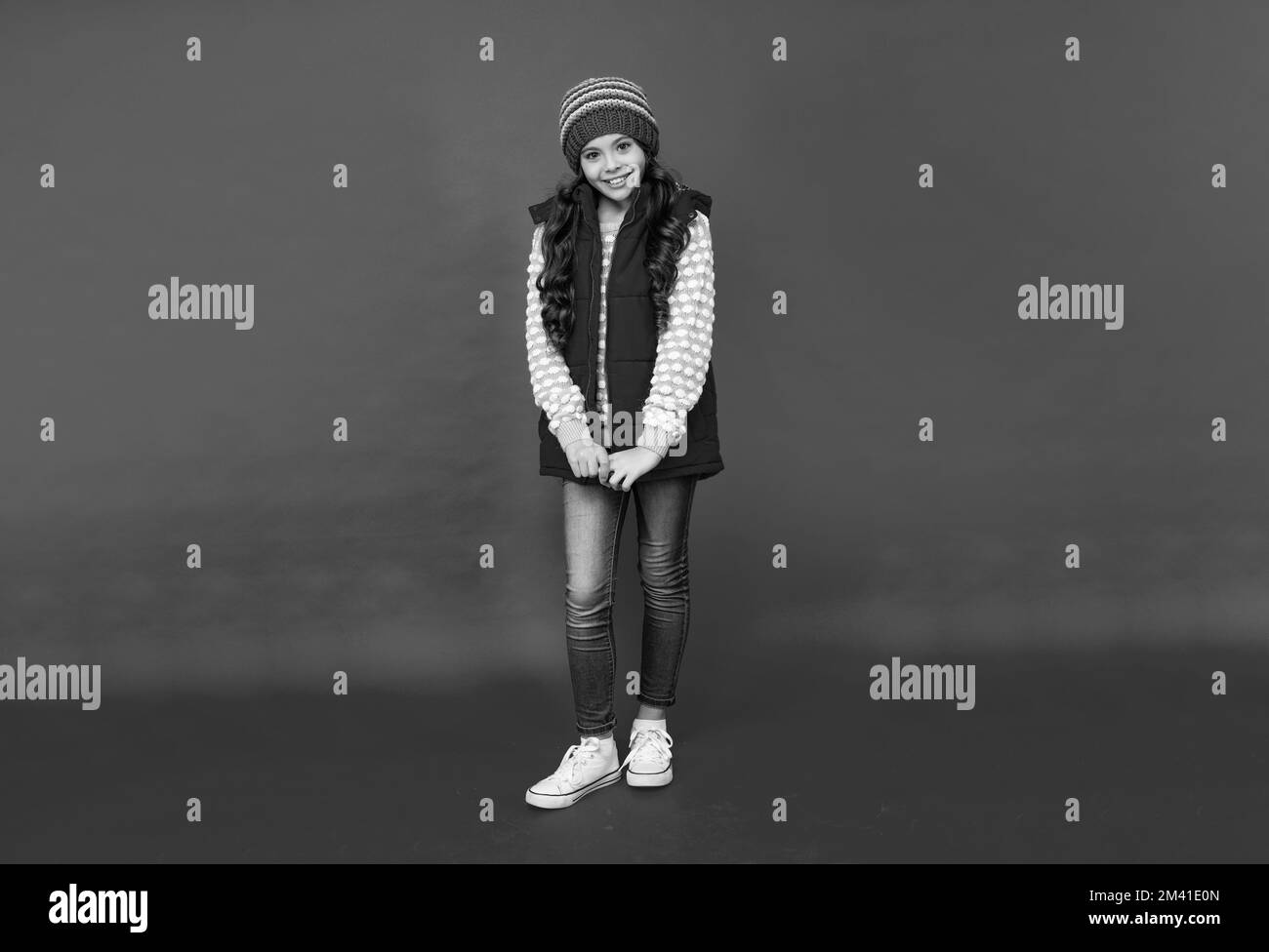 full length of happy teen girl in knitted winter hat and down vest on