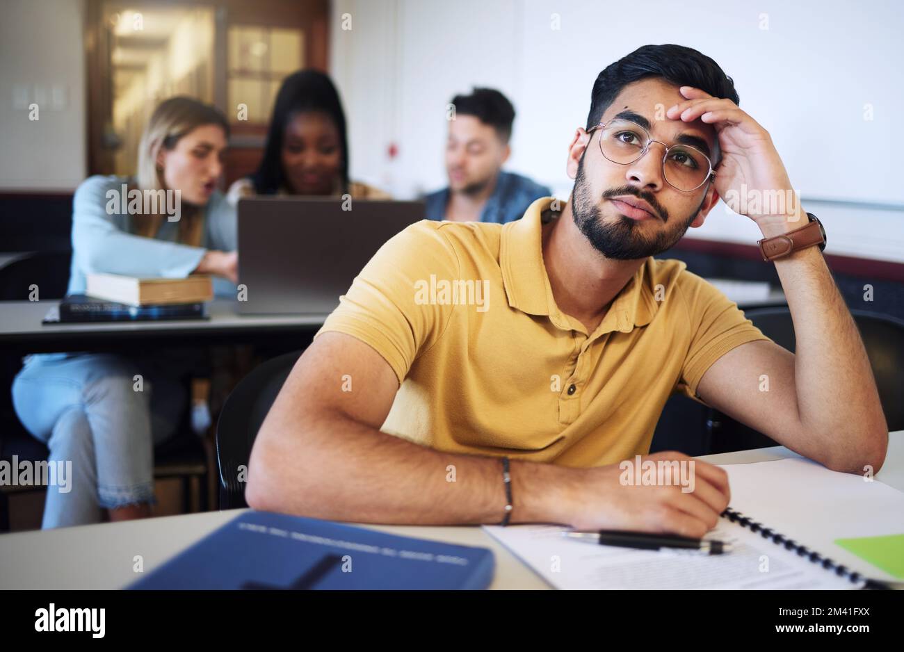 Indian man, student and bored in classroom, tired and stress with notes, examination or task. Young male, guy or exhausted for education, test or Stock Photo