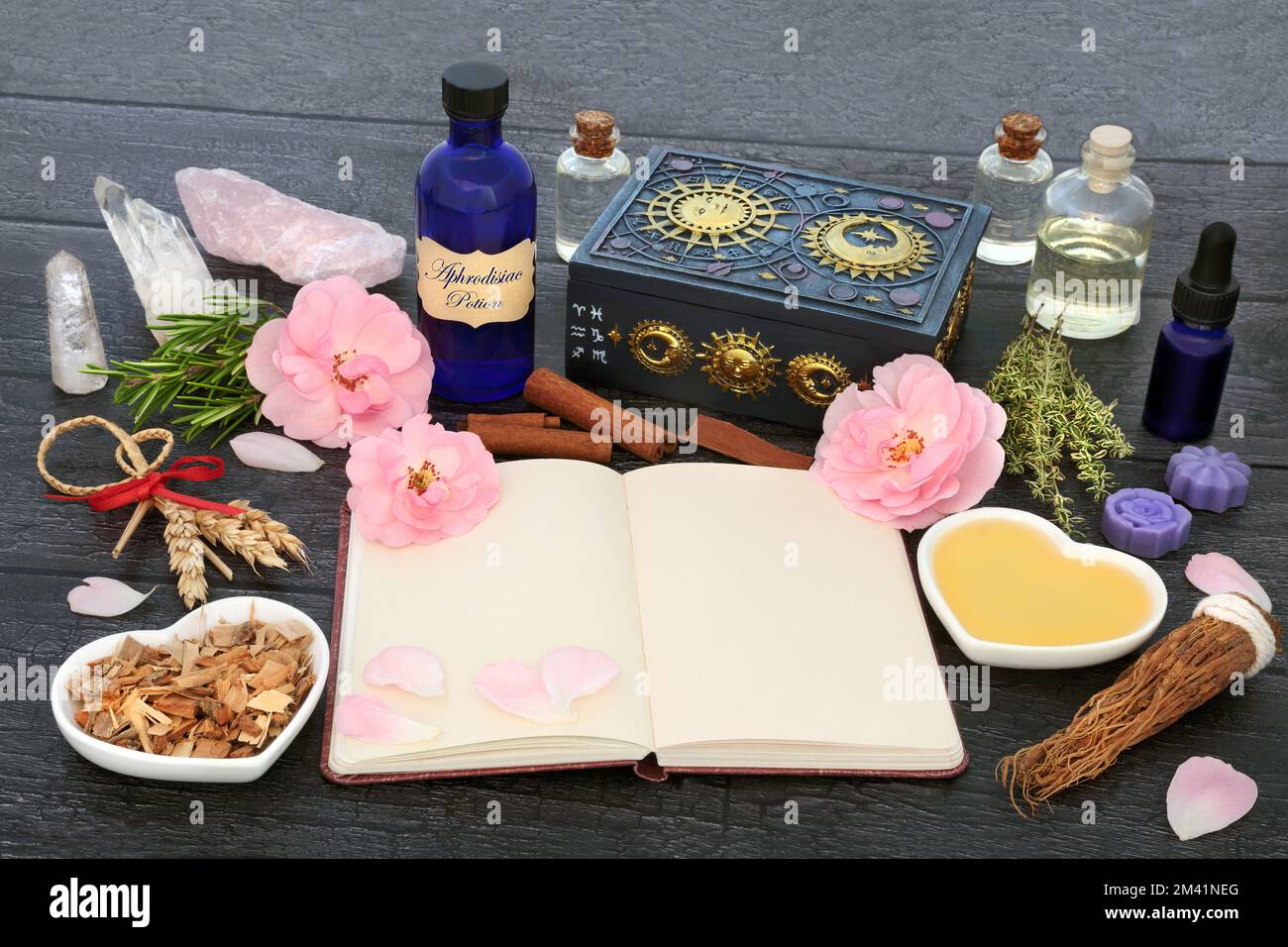 Aphrodisiac love potion recipe ingredients with magic spell notebook  herbs, rose flowers, honey, fertility corn dolly, oil, spring water and crystal. Stock Photo