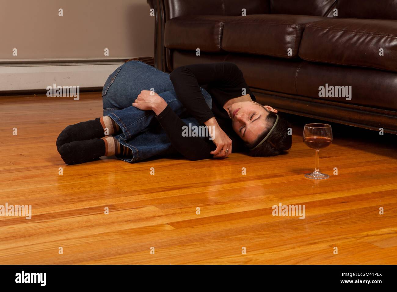 Young woman lying on the floor passed out in the fetal position with a wine glass Stock Photo