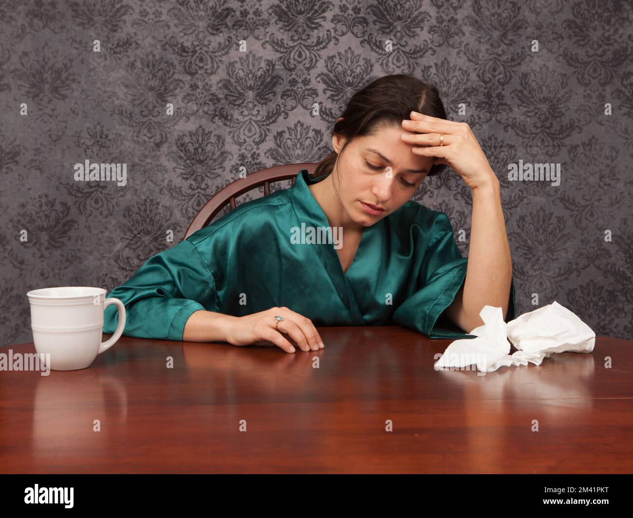 Woman suffering from headache and flu symptoms at home with a coffee cup and tissues Stock Photo