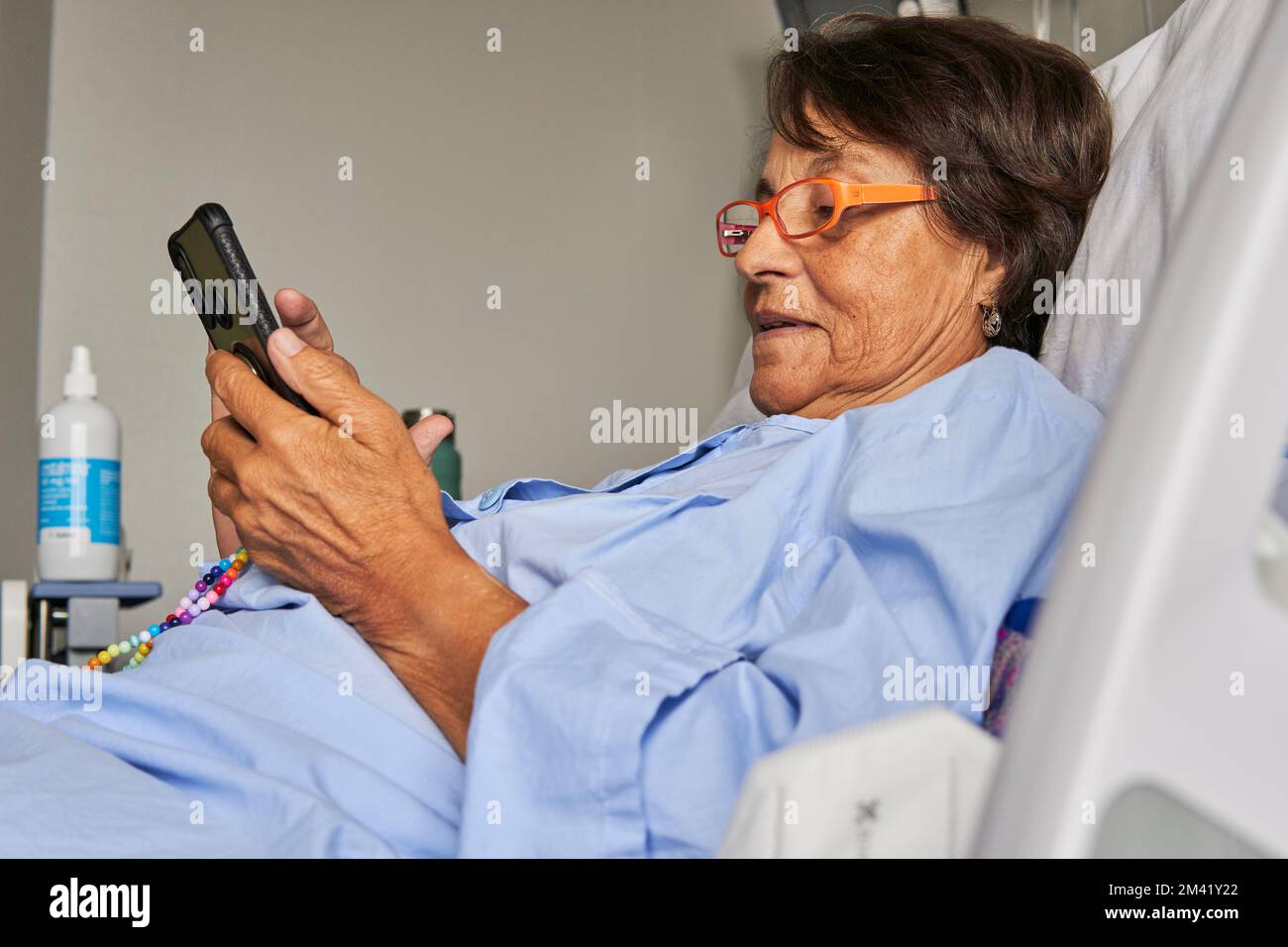 senior lady in the hospital room sitting on the stretcher checking her mobile phone medical attention app Stock Photo