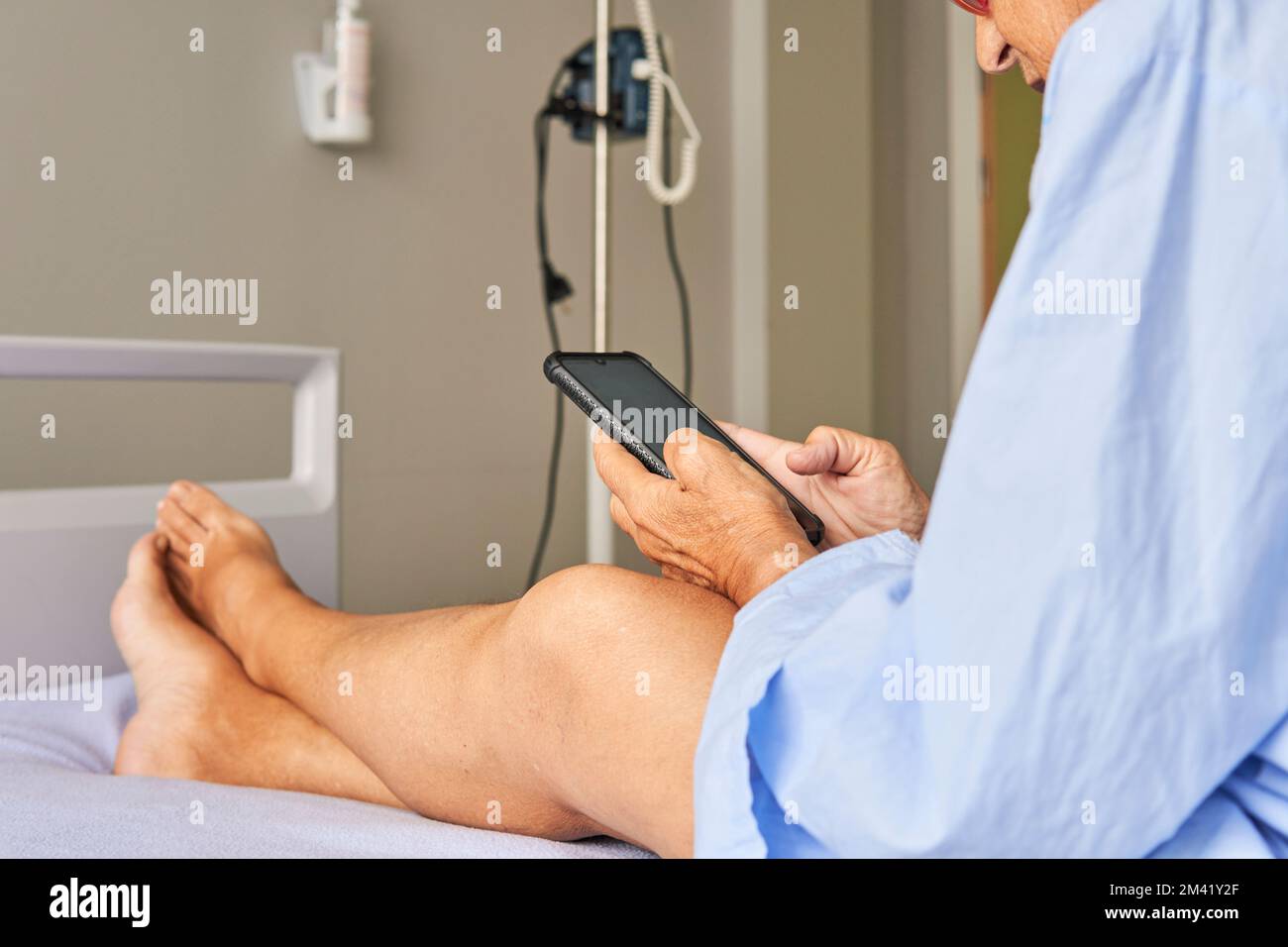 senior lady in the hospital room sitting on the stretcher checking her mobile phone Stock Photo